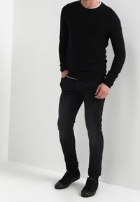 Czarny sweter o fakturze dzianiny z długimi rękawami, w połączeniu z czarnymi, obcisłymi jeansami i czarnymi trampkami. Prosty design, bez widocznych wzorów ani akcentów.