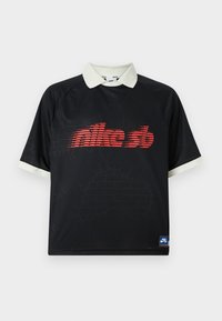 Black polo-style t-shirt with white collar; features red Nike SB logo and subtle brick pattern texture on fabric. Available in relaxed fit.