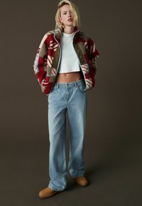 Veste en polaire à motifs rouge, beige et bleu, top court blanc, jeans blue large clair et bottines marron.