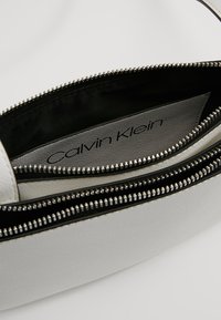 Torebka Calvin Klein o białym, teksturowanym wykończeniu, z czarnym wnętrzem i suwakem w kolorze srebrnym; logo widoczne wewnątrz.