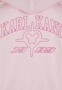 Lyserød hættetrøje med fed, lyserød "KARL KANI" tekst, et hjerteformet logo og "1989" i en grafisk stil nedenunder. Blød stoftekstur.