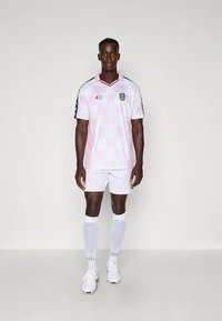 Rosa og hvit rutete fotballtrøye med korte ermer, svarte detaljer og logo. Kombinert med hvite shorts og sokker.