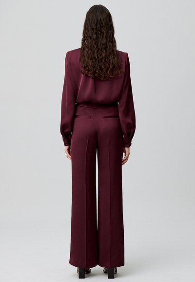 Completo bordeaux composto da una blusa in satin morbido con maniche arricciate e pantaloni a vita alta e gamba larga con tasche posteriori.