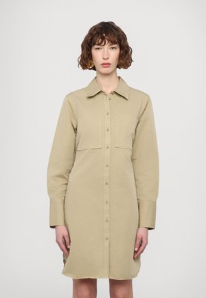 Khaki-pain dugsattu mekko, jossa on pitkät hihat, kaksi rintataskua ja klassinen kaulus. Kangas näyttää sileältä ja siinä on rento istuvuus.