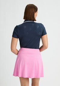 Camisa polo azul marino con un sutil patrón de logotipos y mangas cortas, combinada con una falda rosa claro de corte acampanado con una cinturilla que lleva un logotipo.