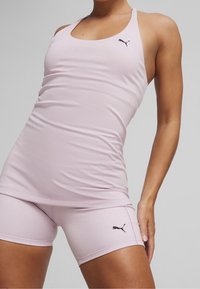 Canotta sportiva e pantaloncini color rosa chiaro, entrambi dal design aderente. Presentano il logo nero Puma sul lato sinistro del petto e sui pantaloncini. Materiale liscio ed elastico.