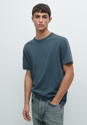 Mørkeblå t-shirt med korte ærmer og rund hals, lavet af blødt materiale. Kombineret med lyse, falmede jeans med en afslappet pasform.