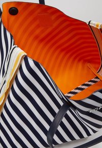 Borsa a tracolla a righe blu e bianche con un interno arancione brillante e manici in pelle nera, aperta per mostrare la fodera interna e la chiusura magnetica.
