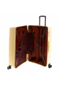 Valigia rigida di colore beige chiaro con una superficie testurizzata. L'interno presenta un ricco rivestimento bordeaux, cinghie incrociate e una tasca con zip.