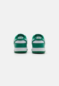 Zelené a bílé tenisky Nike s hladkým koženým svrškem, polstrovaným límcem a bílou mezipodešví. Na patě mají výrazné logo Nike.