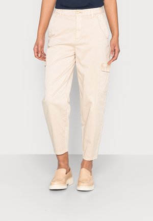 Beige cargobroek met zijzakken, taps toelopende pijpen, zachte katoenen stof en een knoopsluiting, gecombineerd met lichtgekleurde instapschoenen.