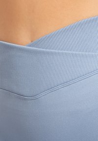Il bordo elastico di colore azzurro chiaro presenta un design rigato, che si trasforma in un tessuto liscio sottostante. Dettagli delle cuciture visibili lungo il bordo.
