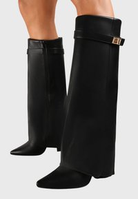 Bottes noires montantes en cuir lisse, avec un bout pointu et une boucle décorative sur la tige, fermées par une fermeture éclair sur le côté.