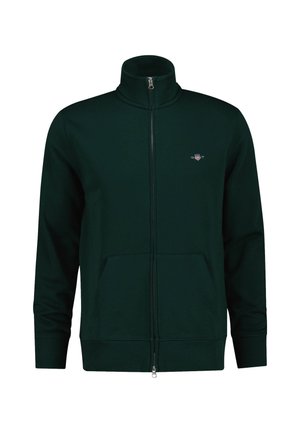 Dunkelgrüne Zip-Jacke mit hohem Kragen, Fronttaschen und gerippten Bündchen. Besitzt ein kleines Logo auf der Brust. Weicher Stoff.