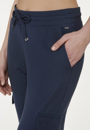 Navy blue jogger pants with a drawstring waist, side pockets, and a smooth, lightweight fabric. Features silver-colored hardware accents.