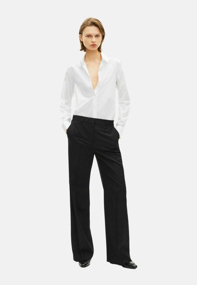 White button-up shirt with a deep V-neck, paired with tailored black trousers, featuring a smooth texture and straight-leg design.