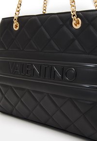Black quilted leather handbag featuring gold-tone chain straps and an embossed brand logo on a smooth leather panel.