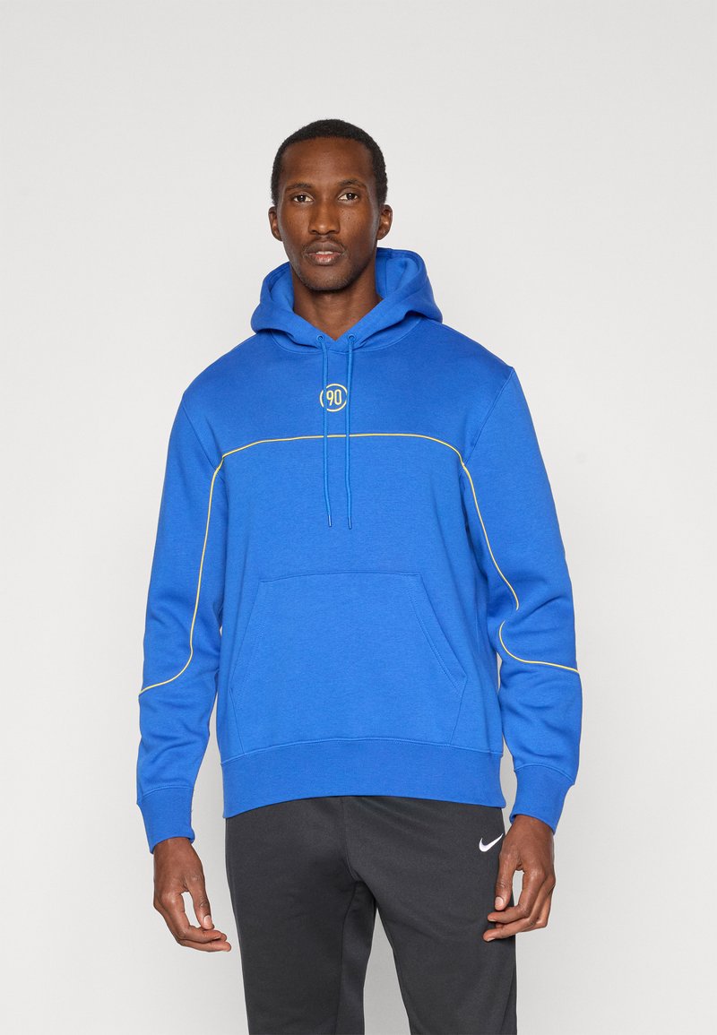 Sudadera azul real con un bolsillo frontal, detalles de costura amarilla y capucha con cordón. Combinada con pantalones de chándal negros que tienen un logotipo.