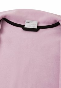 Tessuto rosa chiaro con una morbida texture, caratterizzato da un colletto nero e un'etichetta che recita "Io sono stato qui:" con righe per la personalizzazione.
