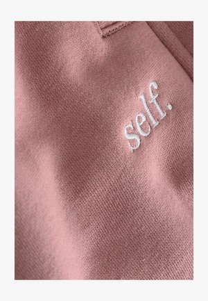 Pink cotton fabric with a soft texture featuring white embroidered text reading "self." on the front side. Simple and minimalist design.
