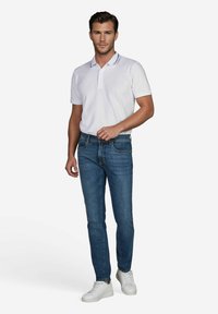 Weißes Polohemd mit kurzen Ärmeln, kombiniert mit blauen Jeans und weißen Sneakers, das eine taillierte Silhouette und einen lässigen Stil präsentiert.