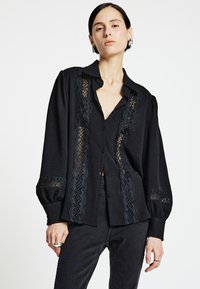 Schwarzes Hemd zum Zumachen mit Spitzen-Akzenten entlang der Vorderseite und der Ärmel, ausgestattet mit einer lockeren Passform, langen Ärmeln und einem klassischen Kragen.