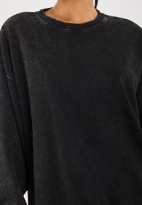 Svart oversized sweatshirt laget av myk, teksturert stoff med rund hals og drop shoulder-design. Slitt finish gir en subtil dybde.