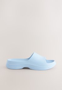 Sandale à glissière bleu clair en caoutchouc lisse, avec un design à bout ouvert, une semelle extérieure arrondie et une esthétique minimaliste.