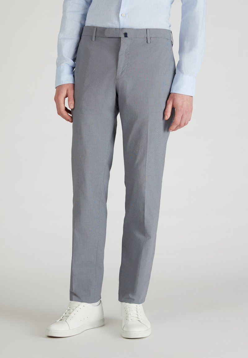 Pantalones gris ajustados con un patrón sutil, corte recto y bolsillos inclinados, combinados con zapatillas blancas para un look casual.