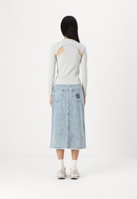 Tricou gri cu mânecă lungă și detalii decupate, asortat cu o fustă din denim de un albastru deschis, ce prezintă broderie florală pe buzunarul din spate.