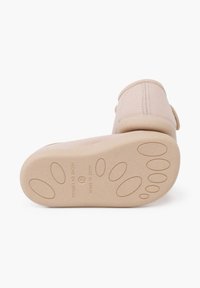 Hellbeige Schuhe mit einer strukturierten Gummisohle, die runde Traktionspunkte aufweist. Genähte Akzente in der Nähe der Ferse, beschriftet mit "Made in Spain."