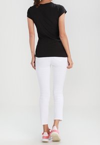 Czarna koszulka z krótkim rękawem w zestawieniu z białymi dopasowanymi dżinsami i sportowymi butami z różowymi akcentami. Prosty design, brak widocznych wzorów, gładka tekstura.