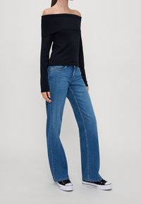 Haut bleu marine à manches longues décolleté épaules avec texture côtelée, associé à un jean large bleu clair et des baskets noires à semelles blanches.