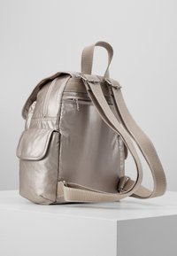 Zaino metallizzato beige con spallacci imbottiti, tasche con zip e finitura testurizzata. Presenta una tasca laterale e cuciture rinforzate.
