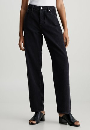 Jeans de mezclilla negros de talle alto y pierna recta con un diseño clásico de cinco bolsillos y detalles de costura sutiles, combinados con sandalias negras de tacón bloque.