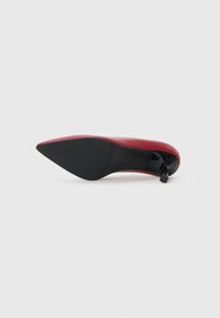 Red pointed-toe high heel shoe with black sole and a small, shiny black heel tip, photographed from the sole side on a white background.