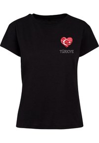 T-shirt en coton noir avec un cœur rouge arborant un motif du drapeau turc et le mot "TÜRKİYE" en blanc dessous le cœur. Manches courtes, col rond.
