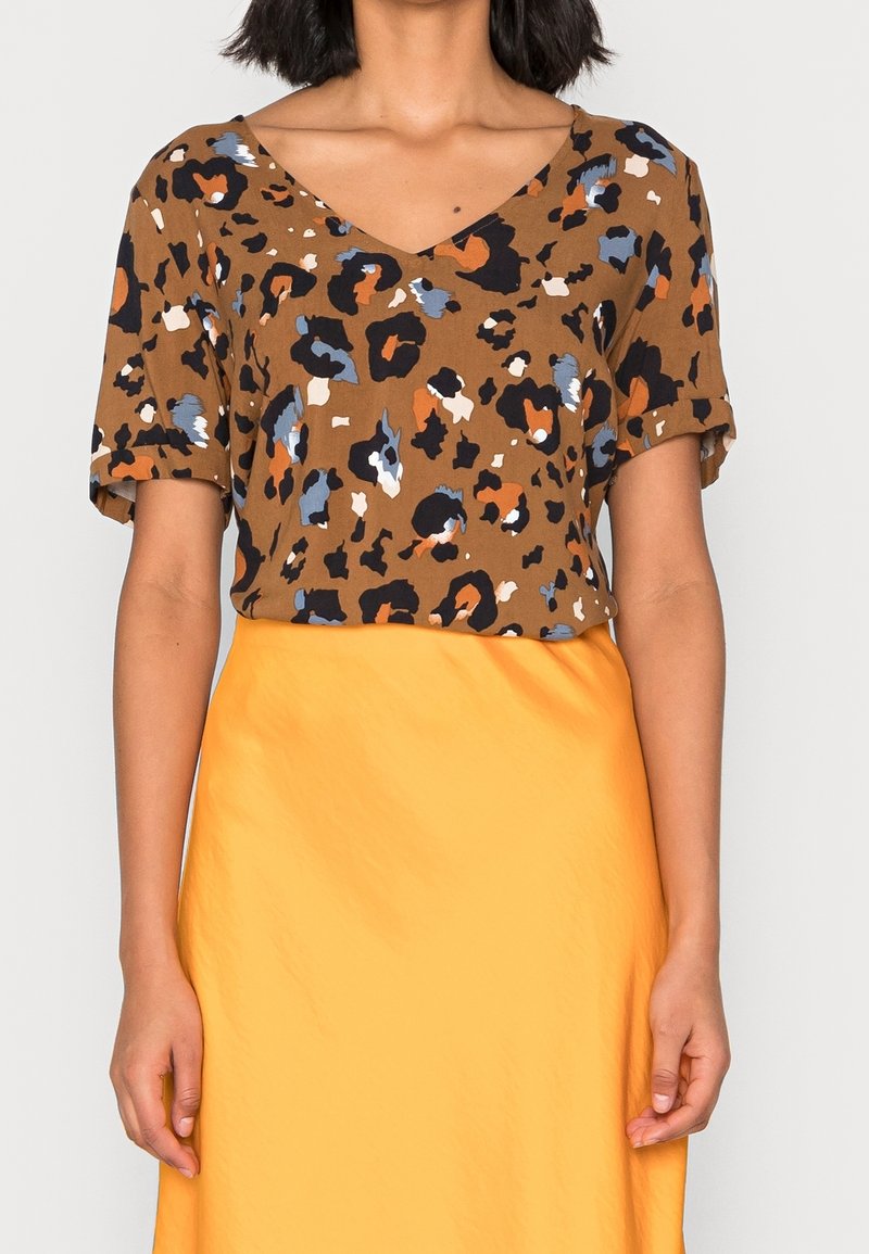 Haut marron à manches courtes avec un motif léopard en orange, bleu et noir. Design en V, associé à une jupe jaune lisse.