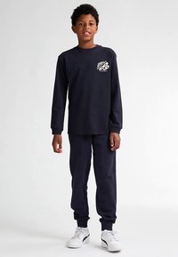 Tummansininen pitkähihainen paita, jossa pieni kuvio vasemmassa rinnassa, yhdistetty vastaaviin verkkarihousuihin. Kangas näyttää pehmeältä; molemmissa on joustavat resorit.