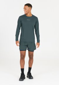 Dunkelgrünes Langarmshirt mit "ENDURANCE"-Logo, kombiniert mit passenden Shorts. Glattes Material, sportliche Passform und Rundhalsausschnitt.
