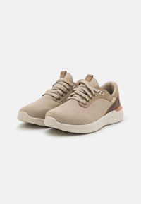 Zapatillas deportivas beige con una parte superior de malla texturizada, ligera amortiguación y acentos marrones en el talón y el lateral.