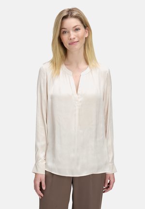 Blusa di seta crema con colletto alla mandarino, maniche lunghe e una leggera lucentezza. Presenta un pronunciato scollo a V e dettagli plissettati.