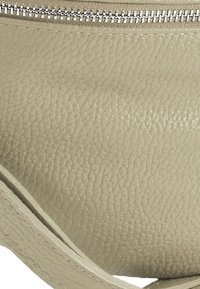 Lichtbeige leren etui met een textuurafwerking; zilverkleurige metalen rits langs de bovenrand; gebogen vorm en minimalistisch ontwerp.