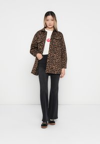 Cappotto leopardato in un tessuto morbido, con colletto e bottoni frontali, abbinato a una t-shirt bianca con grafica e pantaloni neri a zampa.
