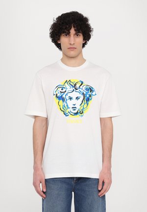 T-shirt en coton blanc avec un graphique bleu et jaune de la tête de Méduse et le texte "VERSACE" en dessous, coupe décontractée, manches courtes.