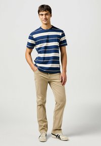 Camiseta de algodón a rayas en azul marino y blanco, combinada con pantalones rectos beige y zapatillas ligeras con detalles en negro.