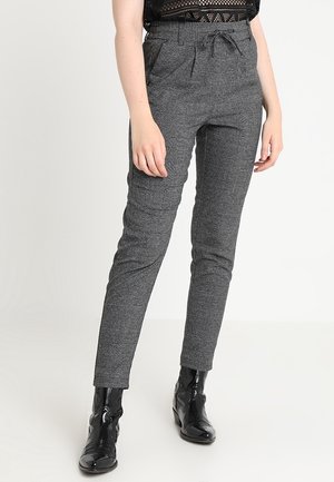 Woman wearing gray plaid tapered pants with a drawstring waist paired with black patent ankle boots and a black lace top.