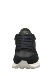 Zapatilla negra con una mezcla de materiales de ante y malla, con una suela de goma blanca y el texto "LAS CHICAS CORREN MÁS RÁPIDO" en la lengüeta.