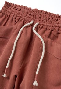 Shorts en lin couleur rouille avec une taille élastique et des détails froncés, ornés d'un cordon tressé blanc noué sur le devant.