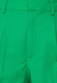 Green lightweight pants with a smooth texture, featuring a flat waistband and subtle contrasting stitching along the seams and pockets.